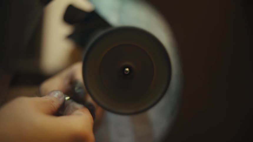 In a softly lit workshop a jeweler carefully holds a gold ring against a rapidly spinning buffing wheel meticulously polishing the metal to a brilliant shine