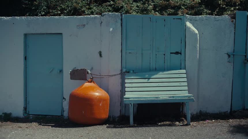 A view of an orange buoy chained to a white wall next to a light blue wooden bench and a matching door