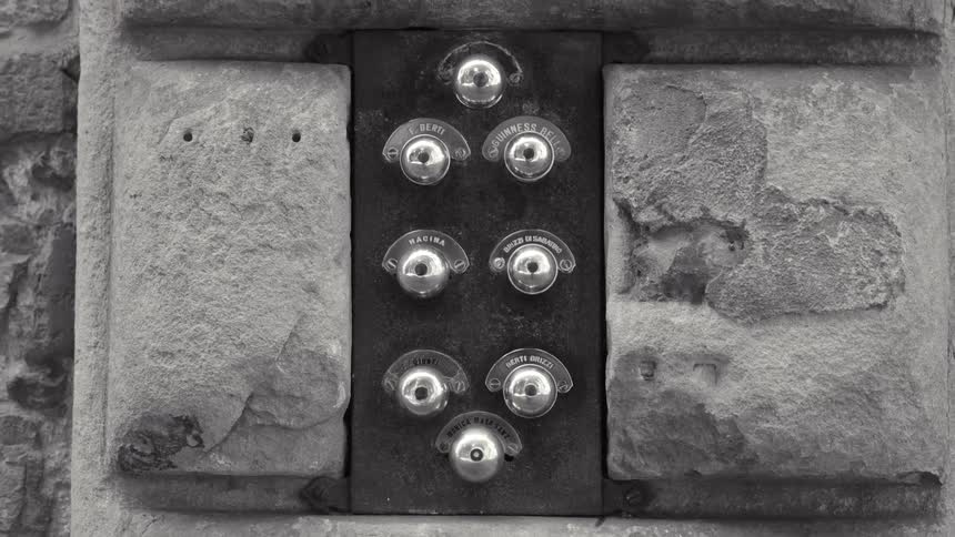 A blackandwhite closeup captures the textured detail of a vintage metal intercom panel with eight round buttons mounted on a rough stone facade