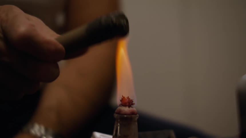 Flame burning on a small container while a hand holds an object above the flame indoors