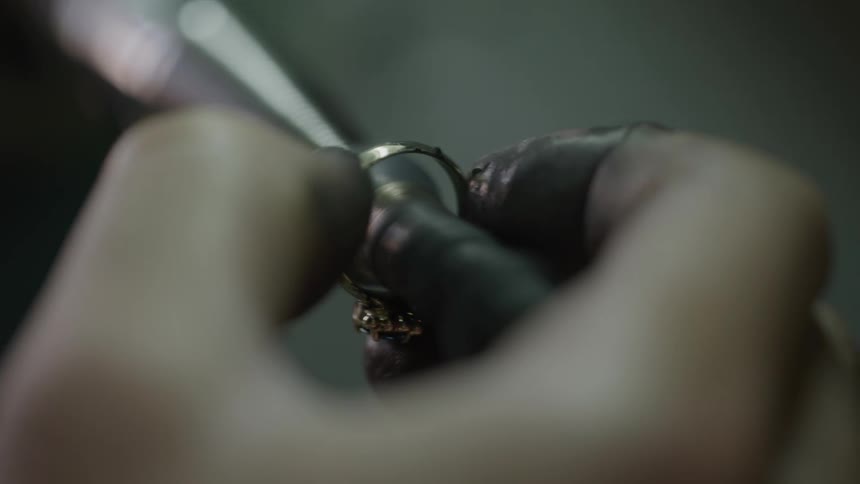 The jeweler is using a tool in his shop to shave a ring