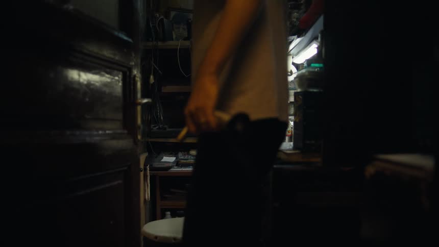 A person walks between shelves while handling tools in a dimly lit workshop