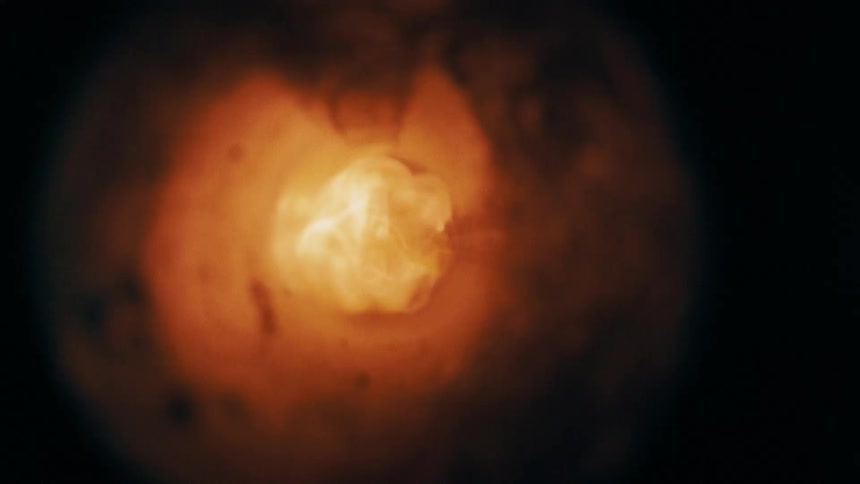 A brilliant spark triggers a fiery blast of combustion sending a turbulent ball of orange flame rolling through a dark enclosed chamber