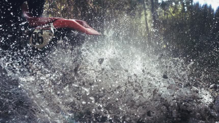 The dirt bike splashes water all over as it speeds through the stream