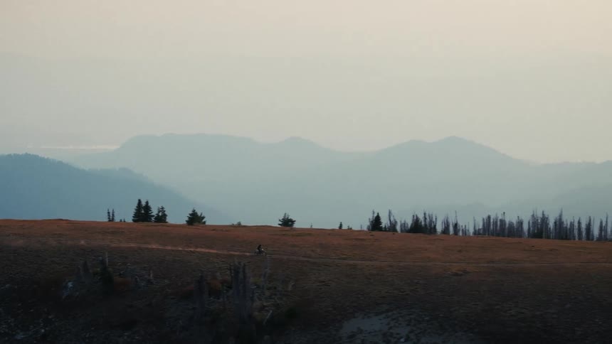 Motocross crosses a plateau with an observation tower and mountains in the background