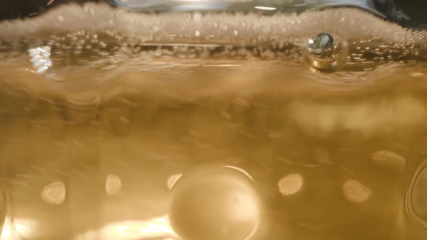 Golden liquid with suspended bubbles and a foam layer near the surface under intense lighting