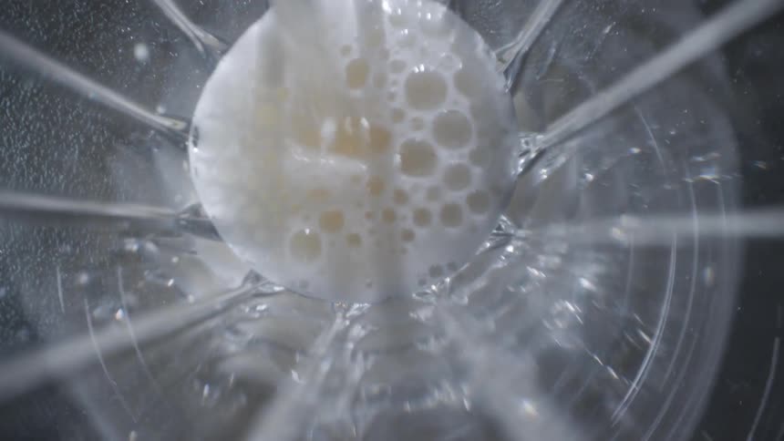 Whitish liquid being poured into the center of a transparent container seen from above