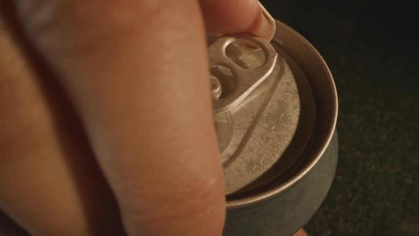 Hand opening the pull tab of a metal can seen in closeup under direct lighting