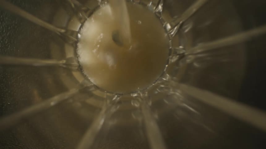Clear liquid being poured into the interior of a transparent container seen from above
