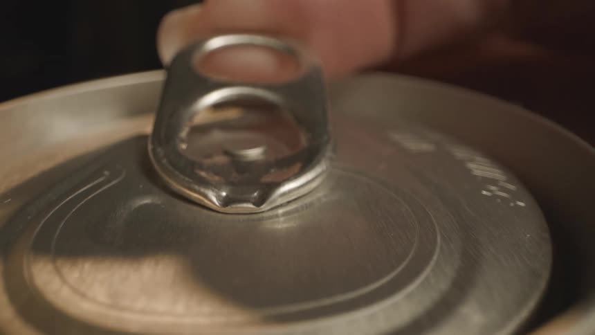Womans finger lifts the tab on a drink can and bubbling liquid emerges