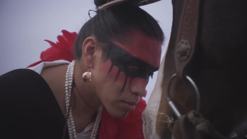 A native american person with red and black face paint greeting a horse in a calm intimate moment