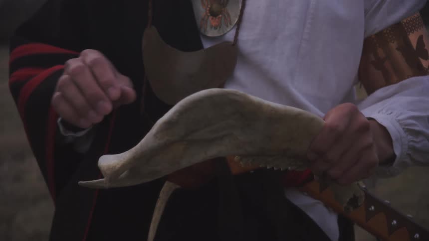 A close view shows the hands of a person wearing traditional clothing holding and examining an animal jawbone