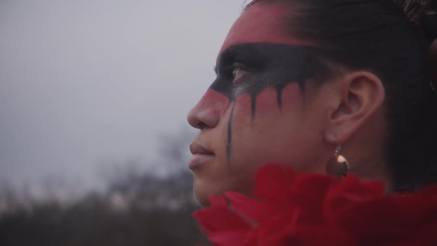 A closeup profile view of an indigenous person with red and black face paint looking into the distance