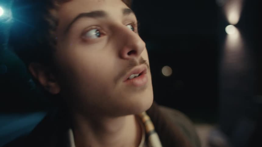 Young teen boy with a mustache standing on a porch then moving forward making a motion to kiss something before he looks to the side and runs away outdoors during night time