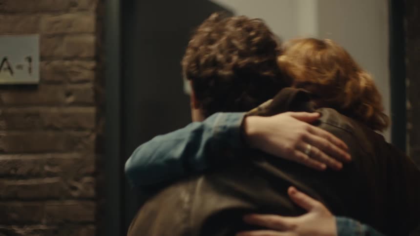 Young man standing at a door holding flowers as a man opens the door and a teenage girl walks outside and hugs him