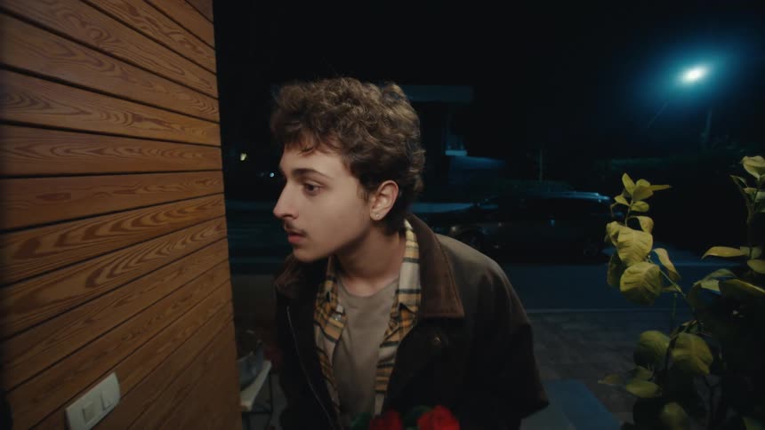 Man holding red flowers while pressing a switch at a residential entrance at night