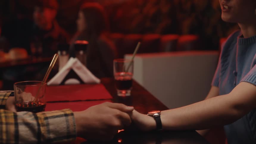 Hands of a couple touching across a restaurant table with warm lighting and drinks in the background