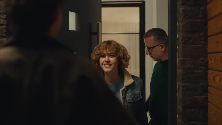 A young man arrives at a door with red roses and is greeted by a man who lets a young woman out to hug him