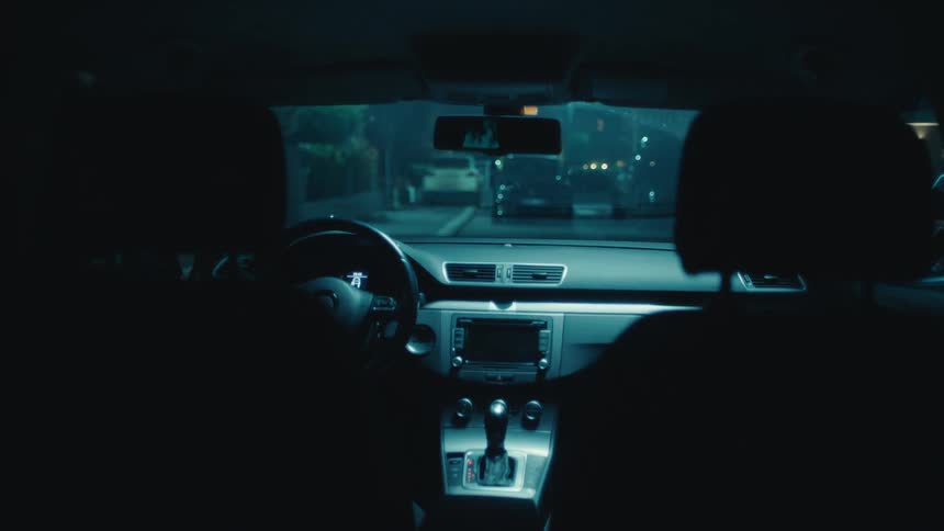 Inside a parked car at night a man attempts to kiss a woman before they exit and walk to the front door of a building