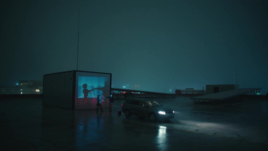 A romantic couple dances beside a car on a rainy dimly lit urban rooftop at night