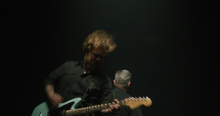Two musicians on stage playing guitars and moving wildly