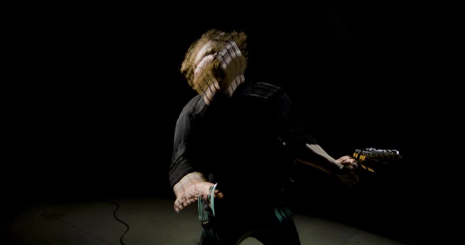 A musician intensely performs on an electric guitar on a dark motion blurred concert stage