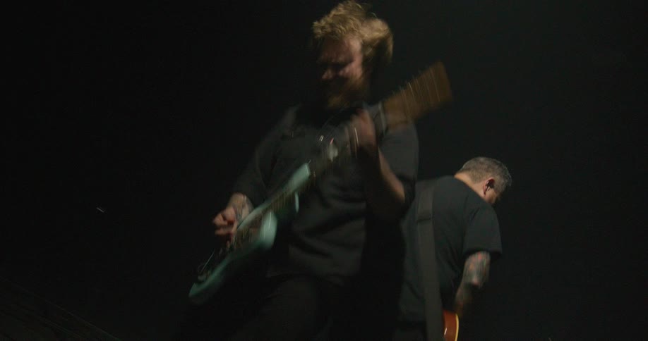 The guitarist in the video has long lightbrown hair and a full beard which he tosses around energetically while headbanging he is playing a light blue electric guitar with a dark pickguard and a woodfinish headstock