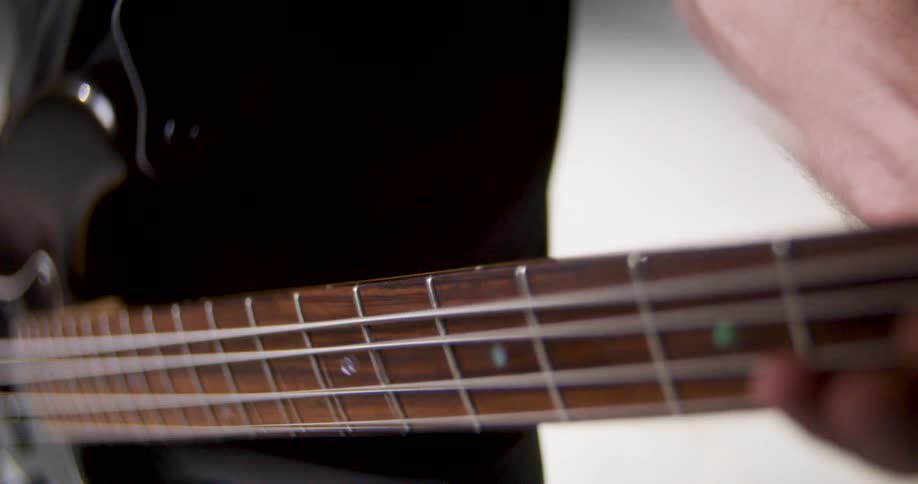 A musicians fingers deftly press down on the metallic strings along the fretboard of a black electric bass guitar highlighting the rhythmic precision of the performance in a detailed closeup