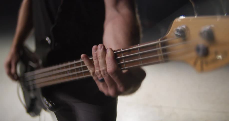 Musicians hand pressing the strings of an electric bass in closeup under directional lighting