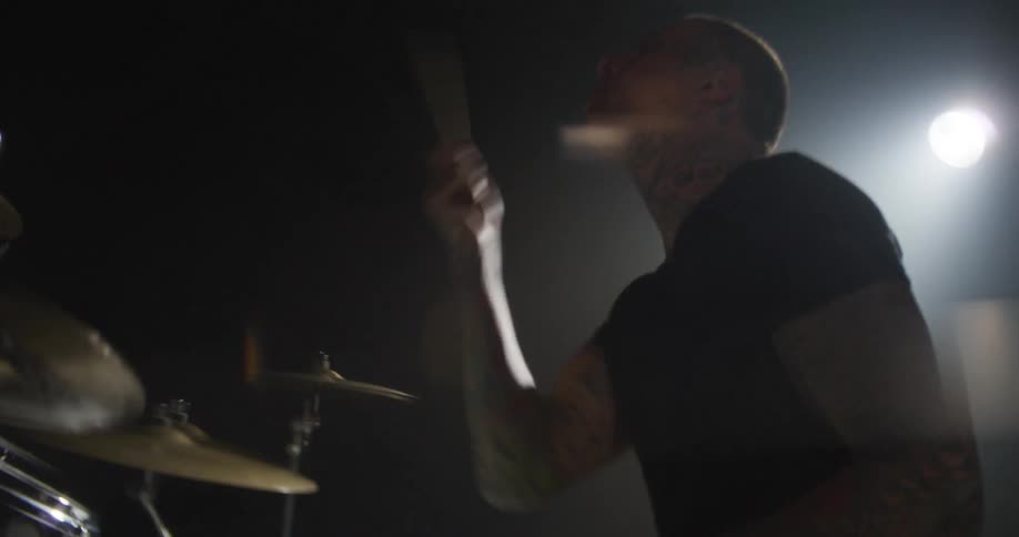 Adult man wearing black clothes playing drums on a stage at a music concert indoors