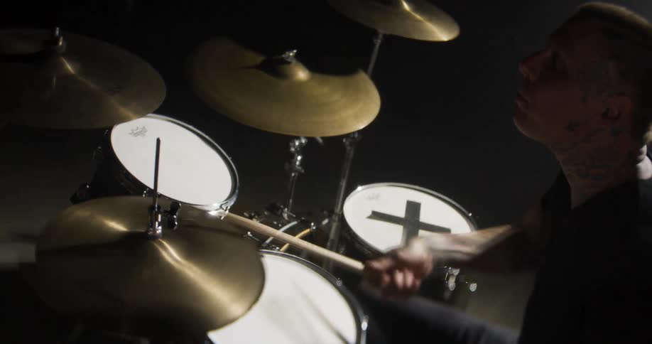 Drummer playing drums with drumsticks in partially lit room