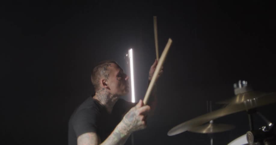 Man holds his drum sticks and swings his arms as he plays the drums