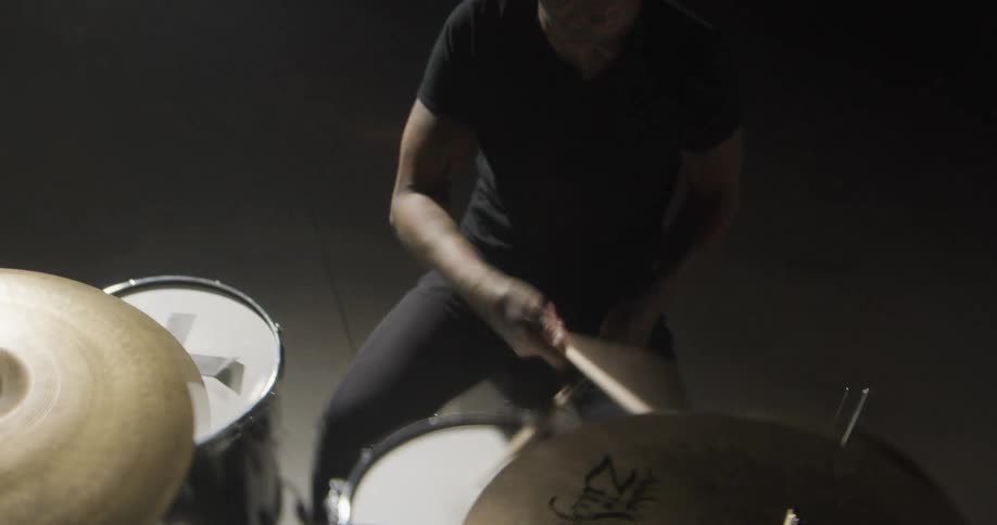 From a dynamic lowangle perspective a drummer in a dark room energetically attacks his drum kit sticks flying in a blur as they crash down on the cymbals and snare