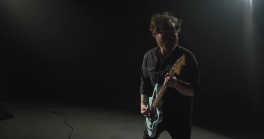 The man jumps up and down while playing the guitar