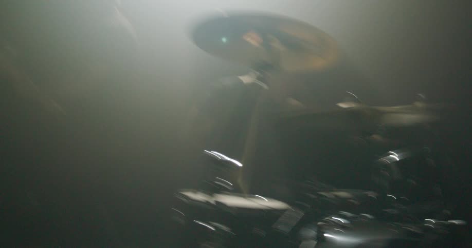 Guitarist and drummer playing together in a dark studio with diffused lighting and partially visible instruments