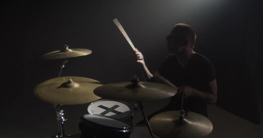 Adult male drummer wearing black clothes playing drums indoors