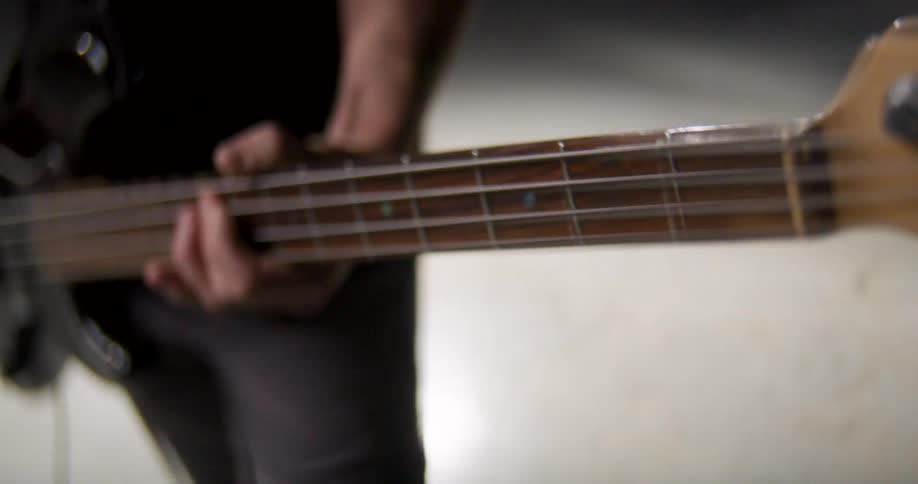 Man stands as he plays a bass guitar