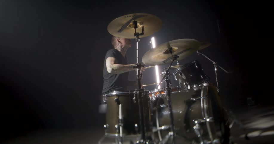 Drummer playing in a dark studio seen in profile with a full drum kit under directional lighting
