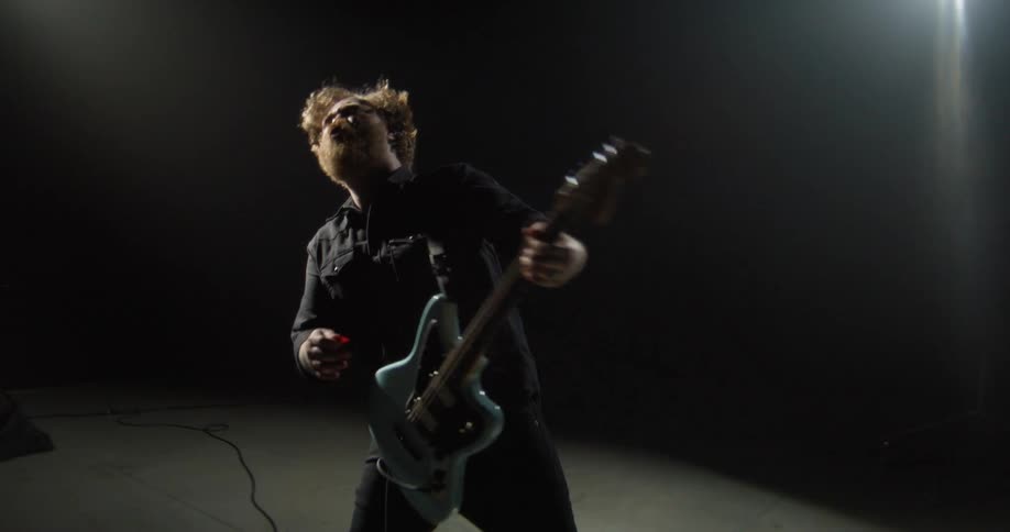 A guitarist plays an electric guitar on a dark concert stage during a live performance