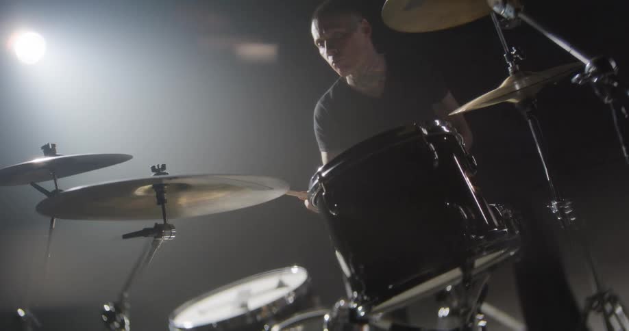 A drummer performs on a drum kit under dim lights during a live concert