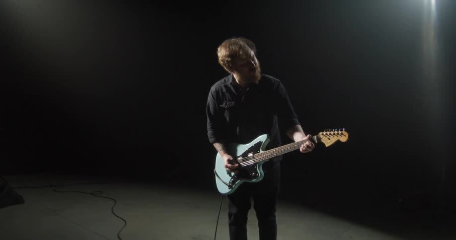A man is alone under a spotlight playing a guitar