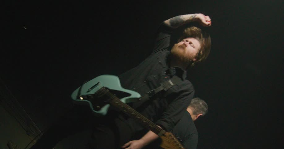 Two men standing and moving as they play guitars