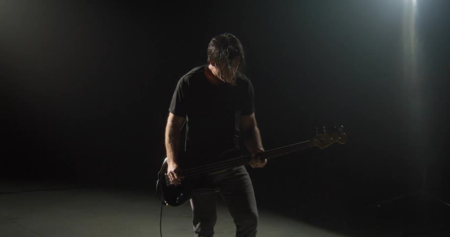 A bassist performs on a dark moody stage silhouetted against the lights