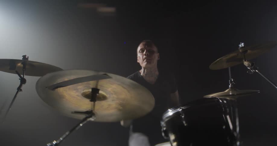 Adult man wearing black clothes playing drums indoors