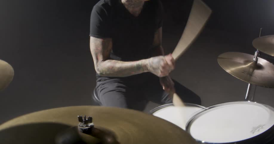 Drummer strikes the drums with sticks in a studio under controlled lighting
