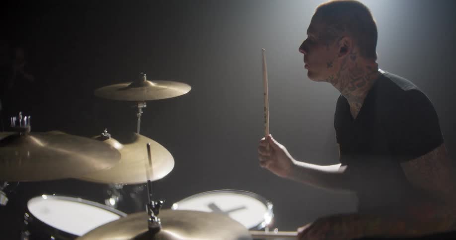 Drummer plays a drum kit in a studio with side lighting and light haze