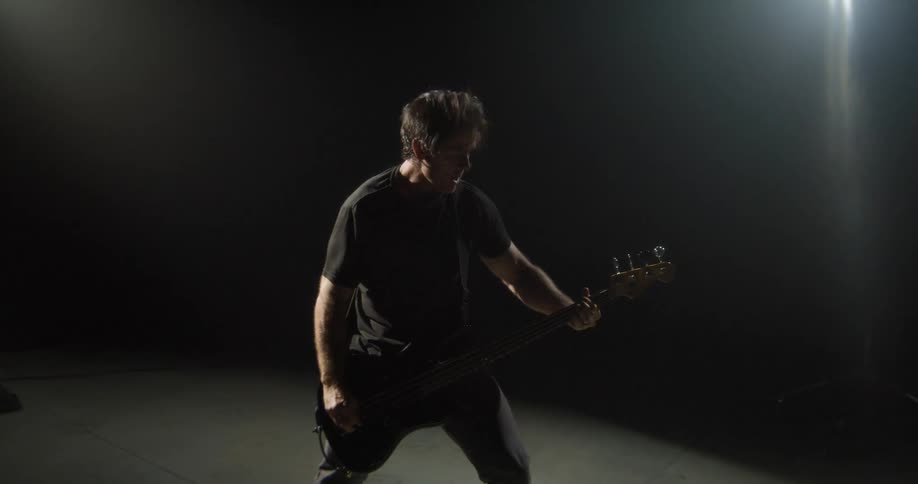 Bassist playing in a dark studio with directional lighting focused on the instrument and the musician