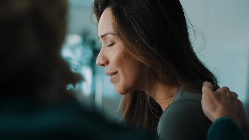 Woman smiling subtly in an indoor setting while receiving a touch on the shoulder