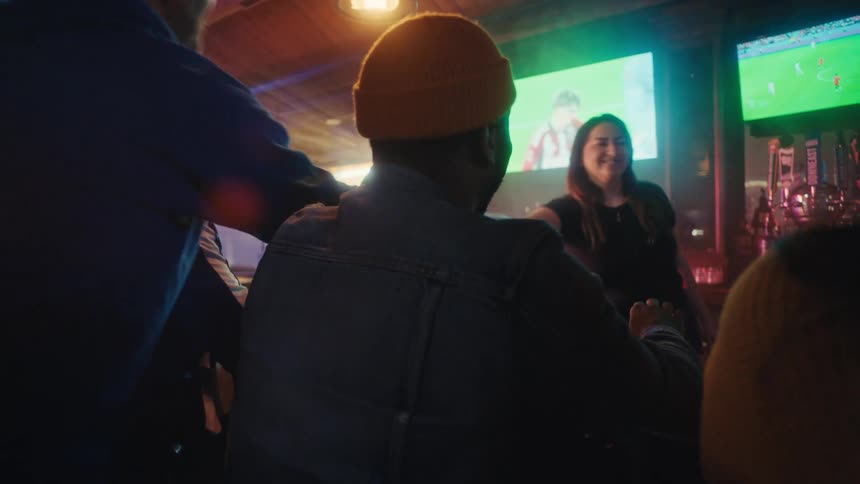 Crowd of people in a bar with a soccer came on television as a bartender hands a person a beer
