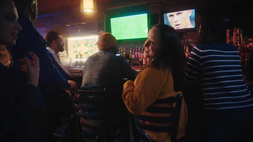 Crowd of people in a bar socializing with a soccer game on the television
